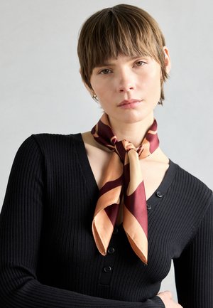 Cachecol de seda com padrões abstratos em tons de bordô e pêssego, amarrado ao redor do pescoço. Sweater preto canelado com detalhes em botões.