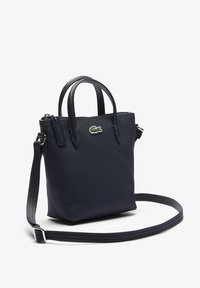 Petit sac à main texturé bleu marine avec deux poignées, une bandoulière longue ajustable, une fermeture éclair et un logo crocodile vert sur le devant.