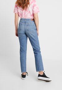 Vaqueros de mezclilla azul claro con piernas rectas, cintura alta y bolsillos traseros. Combinados con una camiseta de tie-dye rosa y zapatillas negras.