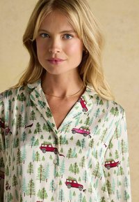Collared shirt featuring a cream background with playful illustrations of green trees and pink and red trucks, made from soft fabric.