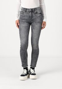 Jean skinny gris taille haute avec un effet délavé, bords effilochés, cinq poches et passants de ceinture, associés à des baskets noires.