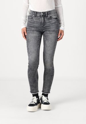 Jean skinny gris taille haute avec un effet délavé, bords effilochés, cinq poches et passants de ceinture, associés à des baskets noires.