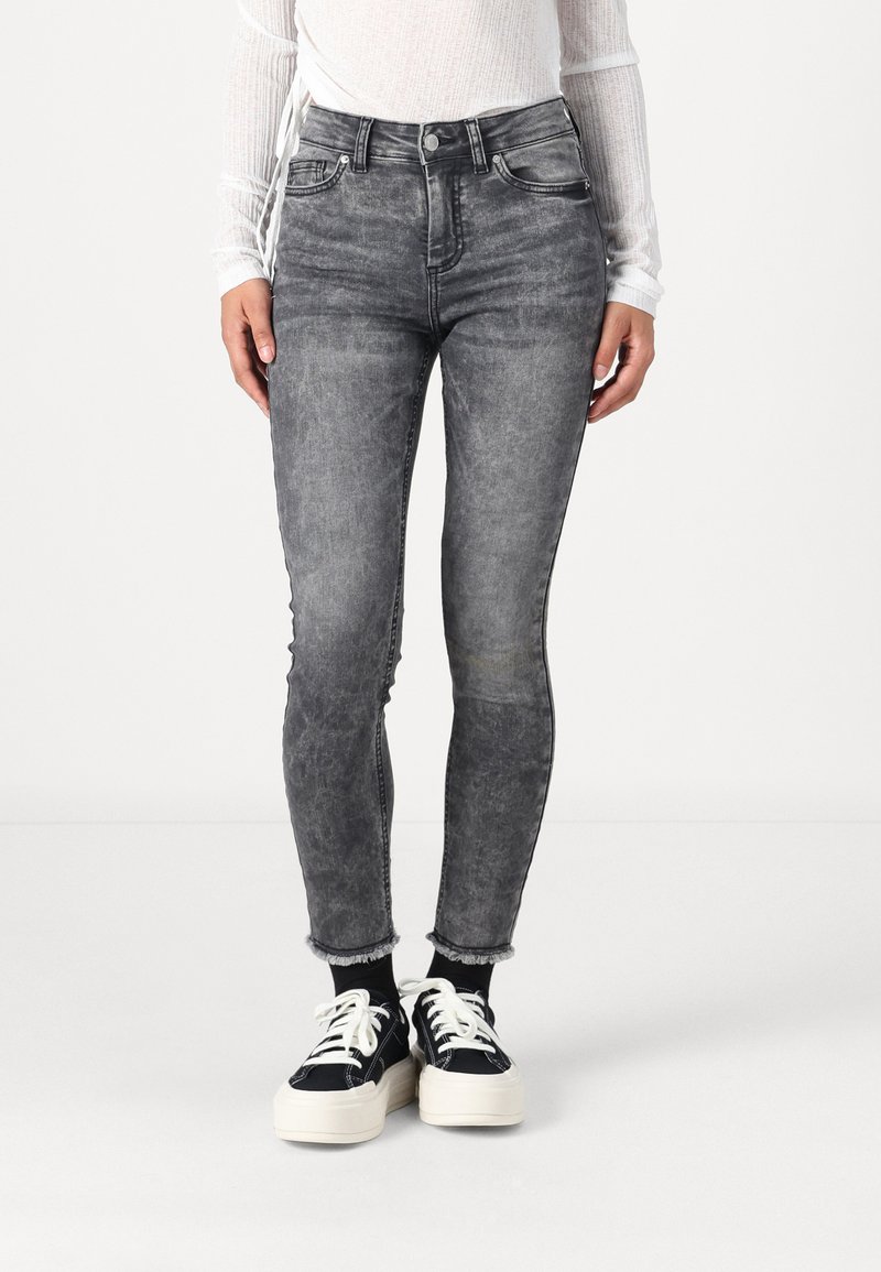 Jean skinny gris taille haute avec un effet délavé, bords effilochés, cinq poches et passants de ceinture, associés à des baskets noires.