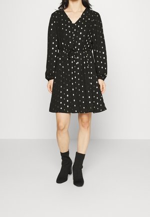 Vestido negro con mangas largas y escote en V, con patrones de puntos plateados, cintura ceñida con lazo, corte relajado y de longitud hasta la rodilla.