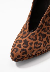 Bottine en daim marron avec un motif léopard, design à bout pointu et côtés découpés, dotée d'une doublure intérieure noire lisse.