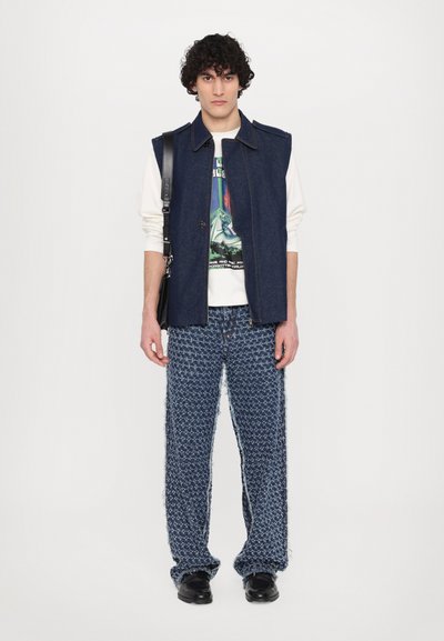 Denim vest with a collar, over a graphic t-shirt. Textured blue patterned wide trousers with frayed edges. Black footwear.