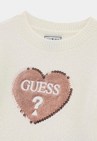 Maglione bianco lavorato a maglia con un grande cuore di paillettes rosa che presenta la scritta "GUESS?" in lettere bianche, bordato da paillettes rotonde e con un collo a coste.