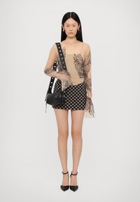 Top trasparente color cammello con ricami neri a forma di foglia, abbinato a una mini gonna nera a scacchi. Accessoriato con una piccola borsa nera e tacchi.