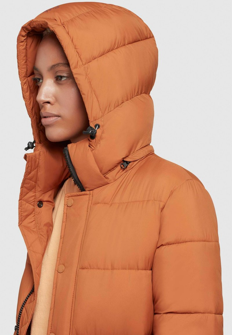 Orangene Pufferjacke mit einer hohen, verstellbaren Kapuze. Sie verfügt über einen Reißverschluss, Knopfdetails und eine gesteppten Textur zur Isolierung.