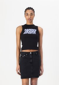 Svart ermeløs cropped topp med dristig hvit "TOMMY JEANS NEW YORK CITY" trykk; kombinert med et høyt liv svart denim skjørt.