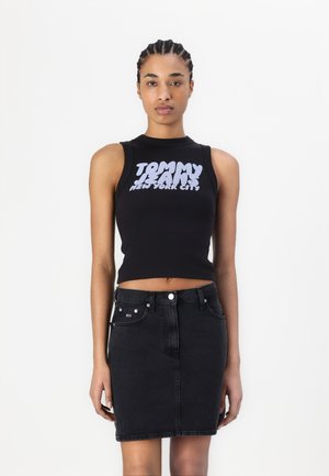 Top corto senza maniche nero con stampa audace bianca "TOMMY JEANS NEW YORK CITY"; abbinato a una gonna in denim nero a vita alta.