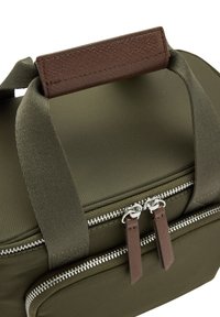 Torba z materiału w oliwkowej zieleni o gładkiej fakturze, wyposażona w brązową skórzaną rączkę oraz podwójne srebrne zamki błyskawiczne z leatherowymi uchwytami.