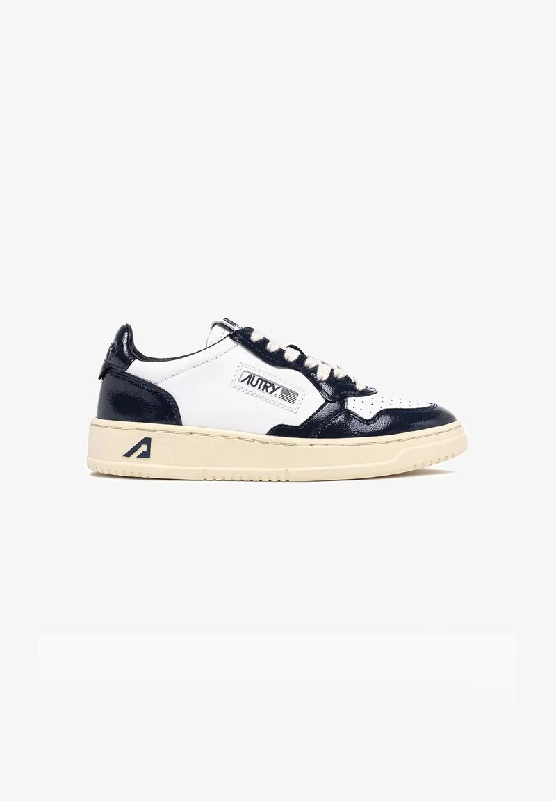 Sneaker in pelle bianca e blu navy con punta traforata, dettagli testurizzati, suola beige e etichetta con marchio sul lato. Design classico a basso profilo.