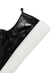 Black leather sneaker with a textured surface, a low-profile design, white rubber sole, and a small loop at the heel for easy wear.