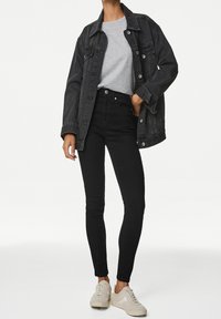 Chaqueta de mezclilla negra sobre una camiseta gris, combinada con jeans negros de tiro alto y zapatillas gris claro. Líneas limpias y silueta ajustada.