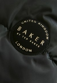 Crni tekstilni komad s kružnim dizajnom, na kojem je utisnut zlatni tekst "BAKER by TED BAKER LONDON" i "UNITED KINGDOM" na kviltanoj pozadini.