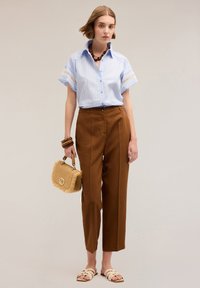 Jasnoniebieska koszula w paski z krótkim rękawem i koronkowym wykończeniem, brązowe spodnie z wysokim stanem, kremowe klapki oraz pleciona torebka w kolorze beżowym.