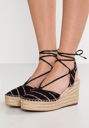 Kile-espadrille-sandaler med sorte stofstropper og ankelbind, med tyk flettet jute-sål og mærketekst på stropperne.