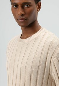Beige gebreide trui met verticale ribbelstructuur, ronde halslijn en korte mouwen, met een licht en ademend ontwerp.