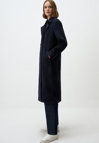 Navyblauwe wollen jas met een rechte snit, knopen aan de voorkant en zijzakken. Gecombineerd met donkere jeans en witte sneakers. Soepele textuur.