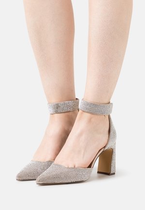 Chaussures à talons hauts argentées à bout pointu, ornées de strass scintillants, avec une bride épaisse à la cheville et un talon carré.