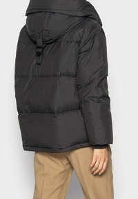 Svart puffjacka med huva, med en quiltad design, tjock vaddering och dragskoavslutning. Slät, glänsande yta.