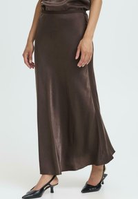 Ruda satino maksi sijonas su lygiu tekstūra ir išplėsta forma, turintis aukštą liemenį ir subtilų blizgesį, derinamas su juodais aukštakulniais batais.