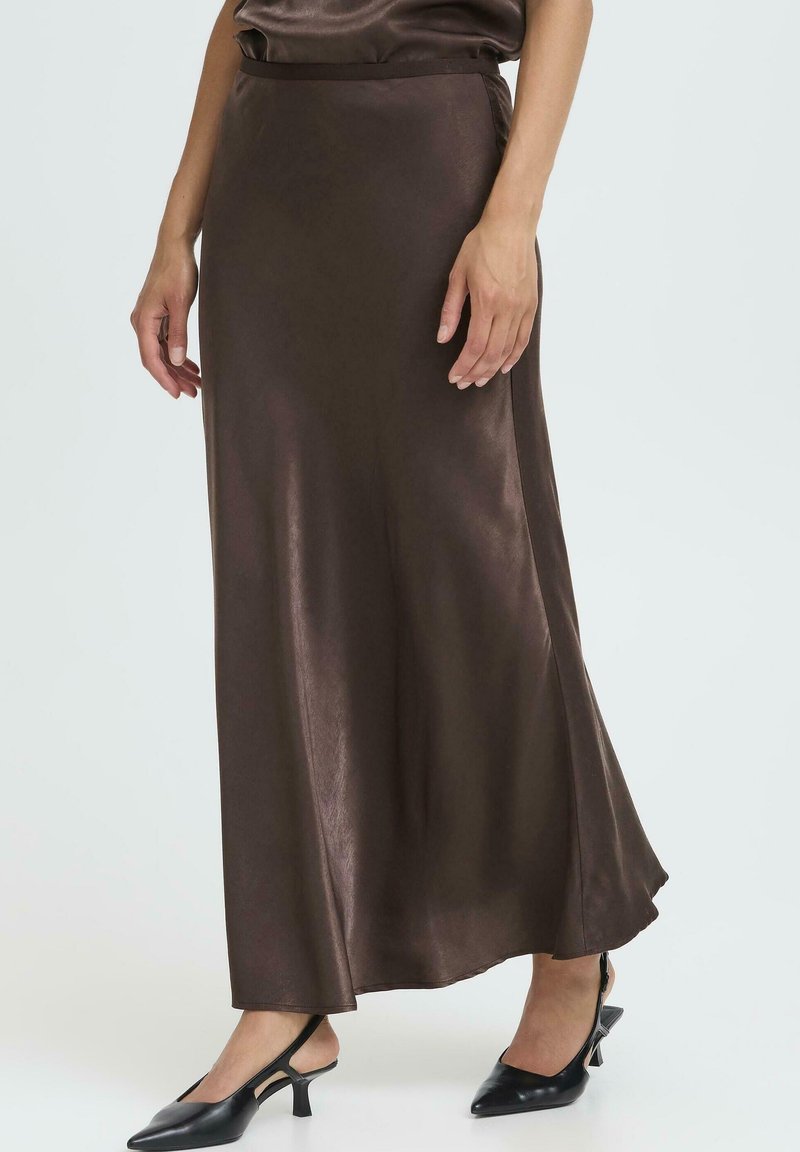 Ruda satino maksi sijonas su lygiu tekstūra ir išplėsta forma, turintis aukštą liemenį ir subtilų blizgesį, derinamas su juodais aukštakulniais batais.