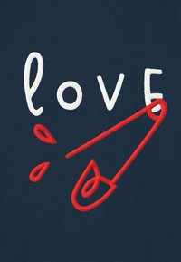 Das Wort "love" in weißer Stickerei mit einer roten Sicherheitsnadel, die das "v" ersetzt, auf dunkelblauem Stoff, mit kleinen roten Tropfen in der Nähe der Nadelspitze.