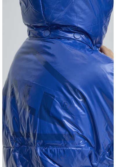 Kék pufferek jéger, fényes, sima felülettel, patentos záródással és diszkrét logónyomattal a hátsó részen.