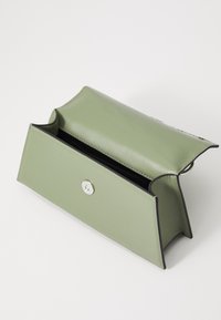 Πράσινη δερμάτινη τσάντα με δομημένο σχέδιο, διαθέτοντας ασημένια κούμπωμα και αντίθετη μαύρη ραφή. Ανοιγμένη με ορατό εσωτερικό.