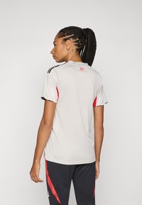 Lichtgrijs sportshirt met korte mouwen, met rode accenten op de schouders en zijkanten. Zwarte strepen langs de mouwen zorgen voor contrast.