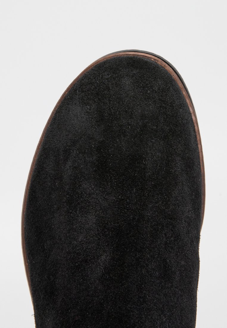 Schwarze Wildlederstiefel mit runder Zehenpartie, ausgestattet mit einer glatten Ledersohle und minimalen Nähten, vor einem neutralen Hintergrund.