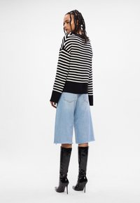 Sweater listrado em preto e branco, calções de ganga largos em azul claro e botas de verniz pretas até ao joelho. Contraste de cores e texturas proeminentes.