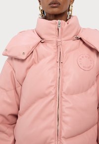 Rosa puffjacka med hög krage, kraftig textur och logotypklistermärke. Har en central dragkedja och överdimensionerade fickor med lock. Metallisk guldfinish.