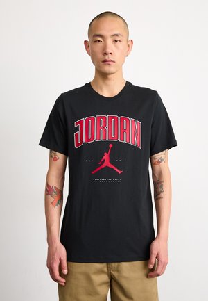 Fekete pamut póló nagy piros "JORDAN" felirattal és egy ugró alak piros sziluettjével. Kerek nyakú és rövid ujjú.