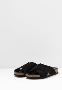 Ciabatte nera in suede con suola in sughero, caratterizzate da un design a strap incrociate e punta aperta, che offrono una finitura testurizzata e un look casual.