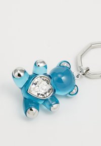 A blue teddy bear keychain made of glossy material, featuring a heart-shaped clear jewel and silver accents on ears and feet.