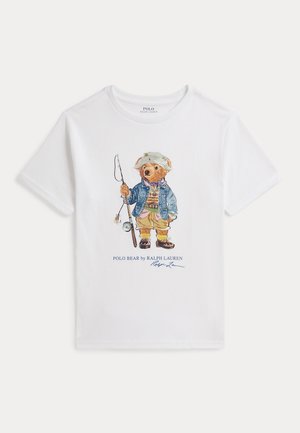 Biała koszula z krótkim rękawem z grafiką niedźwiedzia ubranego w codzienny strój wędkarski, trzymającego wędkę, oznaczona napisem „Polo Bear by Ralph Lauren.”