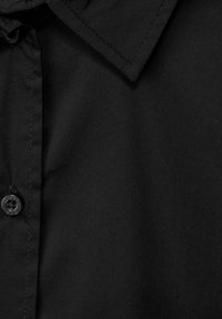 Camicia nera con bottoni, caratterizzata da un colletto a punta, una texture liscia e un bottone visibile nella patta, con dettagli di cucitura.