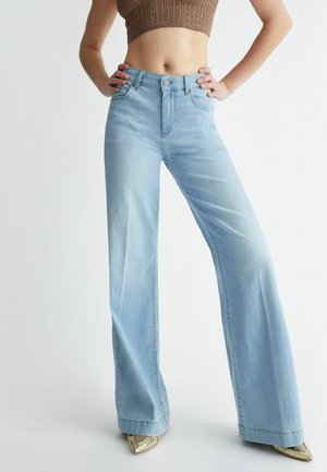 Jeans de tiro alto en azul claro con un corte de pierna ancha, que cuentan con cinco bolsillos y una sutil textura deslavada. Combinados con tacones metálicos puntiagudos.