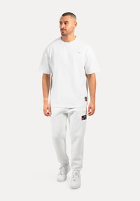Vit bomullsoversize t-shirt med korta ärmar, tillsammans med matchande joggers med svarta detaljer och en logotypklistermärke på sidan.