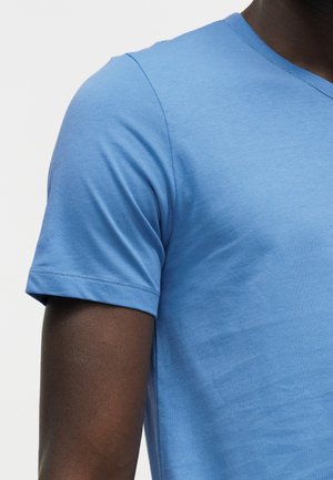Close-up van het bovenlichaam en de arm van een persoon die een effen lichtblauw T-shirt met korte mouwen en V-hals draagt.