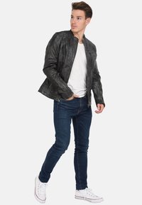 Chaqueta de cuero negra con detalles texturizados, cremallera frontal y cuello mandarín. Combinada con jeans de mezclilla azules ajustados y zapatillas blancas.
