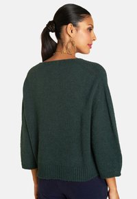 Dunkelgrüner gestrickter Pullover mit weitem Ausschnitt, 3/4-Ärmeln und geripptem Saum. Die strukturierte Stoffoberfläche verleiht dem Design Tiefe.