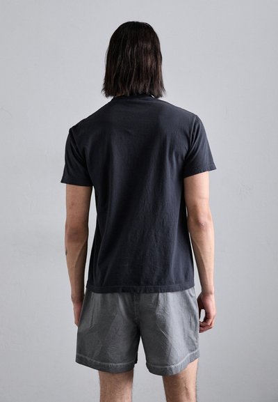 Sort bomulds t-shirt med korte ærmer, ensfarvet design, afslappet pasform, båret med grå shorts, vist fra ryggen mod en neutral baggrund.