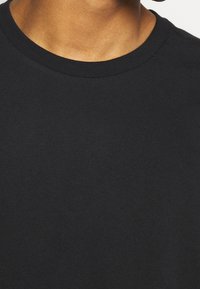 Czarny bawełniany T-shirt z okrągłym dekoltem, gładką teksturą i lekką tkaniną. Brak widocznych wzorów, akcentów ani elementów metalowych.