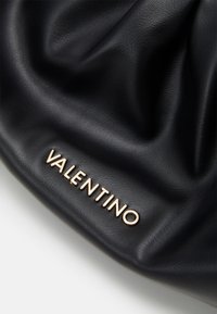 Svart läderväska med rynkad textur och en guldtonad "Valentino"-logotyp accentuerad längst ner. Slät finish.