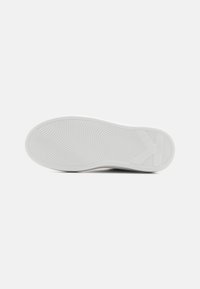 Hvid sneakersål med et struktureret, bølget mønster og logo. Har en rund tå og flad profil. Glat gummimateriale.