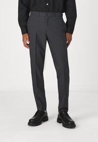 Mörkgrå skräddarsydda byxor med ett subtilt mönster, med knappstängning och sidofickor, ihop med svarta snörskor.